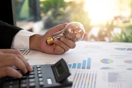 Business owner holding a lightbulb with pennies in it calculating bills